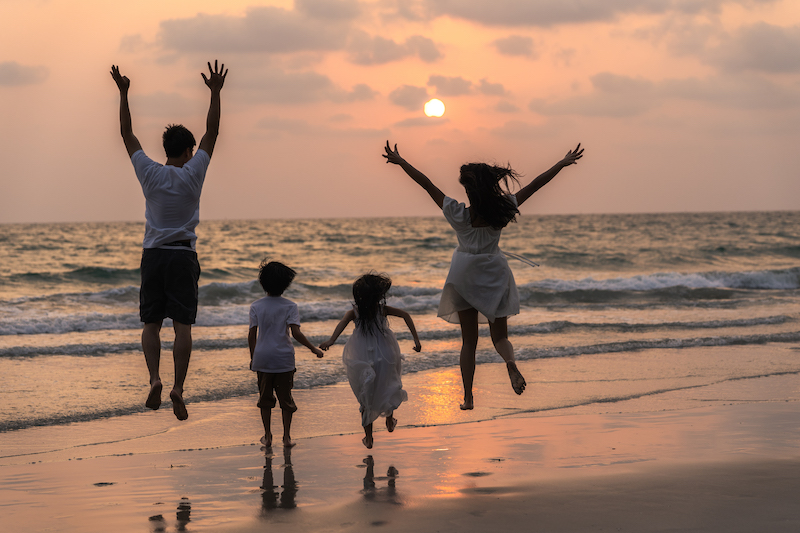 Asian young happy family enjoy vacation on beach in evening. Dad, mom and kid relax running together near sea while silhouette sunset. Lifestyle travel holiday vacation summer concept.